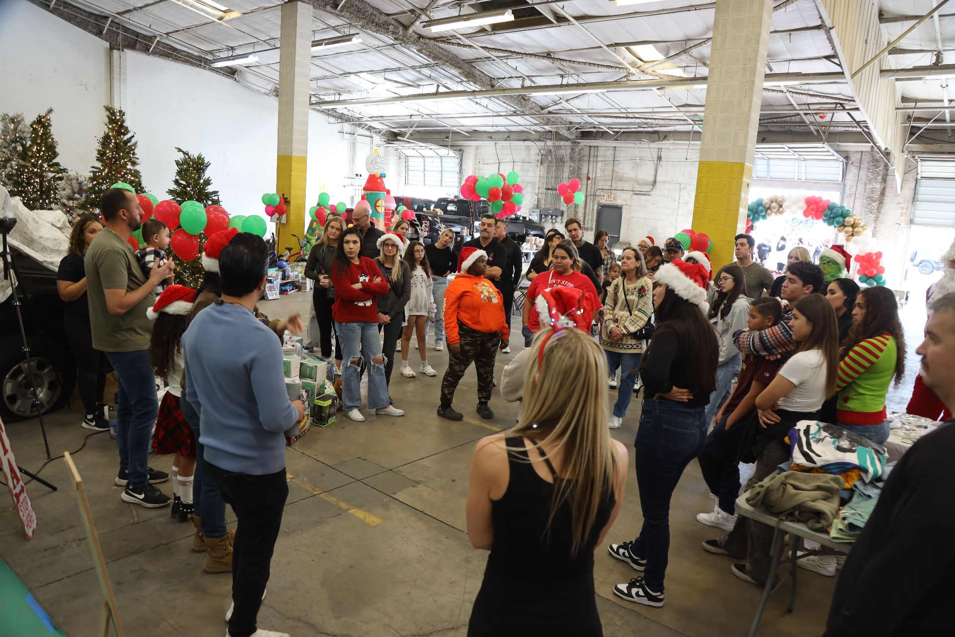 A big crowd of families and volunteers gathered in a warehouse decorated with balloons and Christmas trees at a CARE holiday event