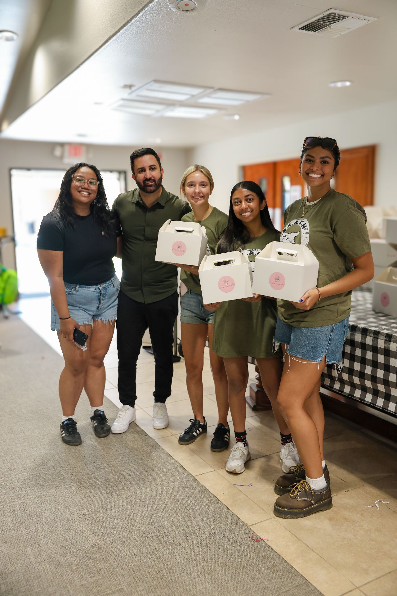Smiling CARE volunteers holding boxed meal kits, ready to hand out to families