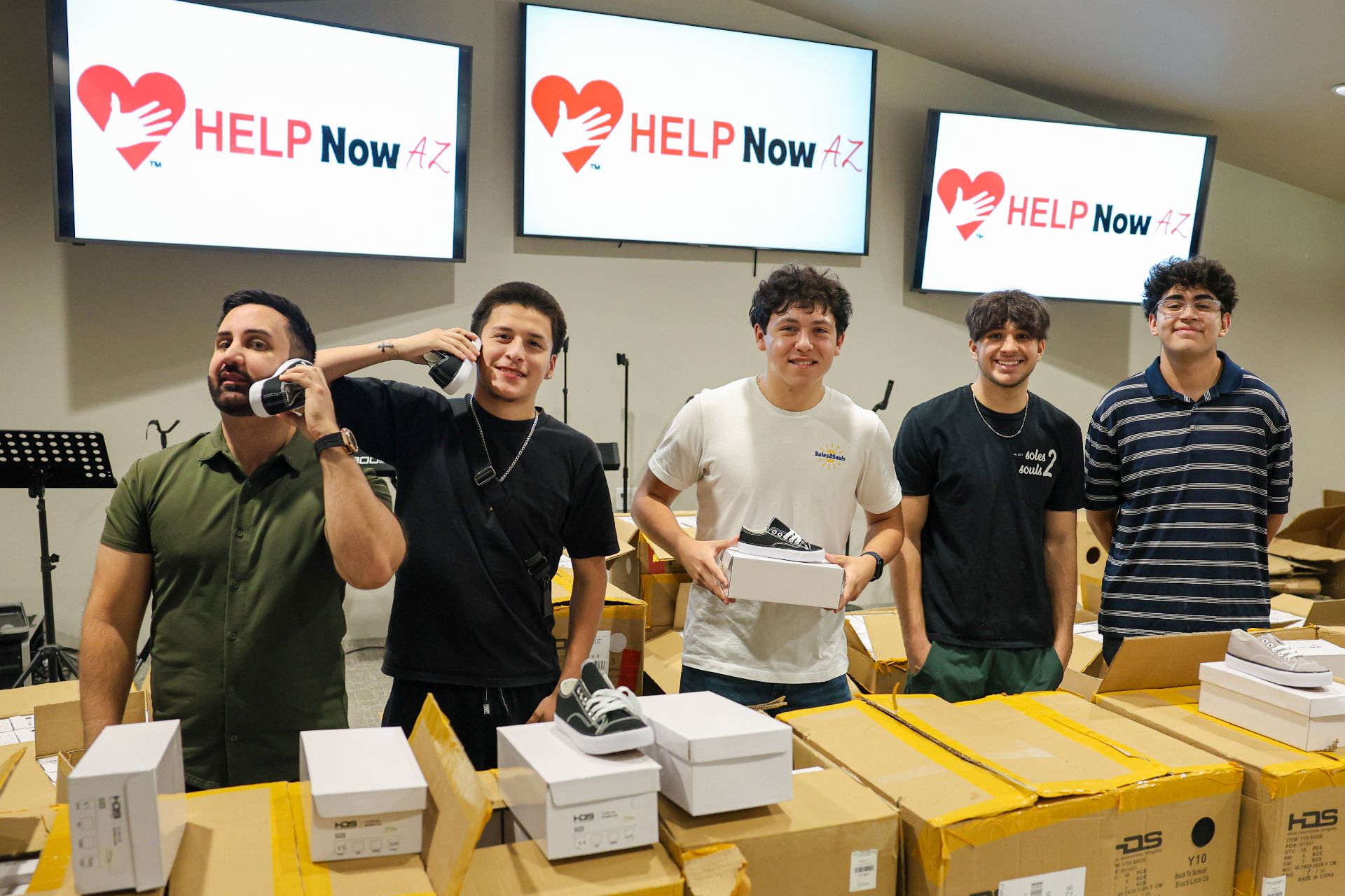 Young volunteers smiling behind a table stacked with boxes of new shoes