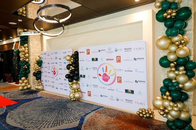 The step-and-repeat backdrop at the CARE 2025 Gala, covered in sponsor logos around the CARE hand, between green and gold balloon columns.