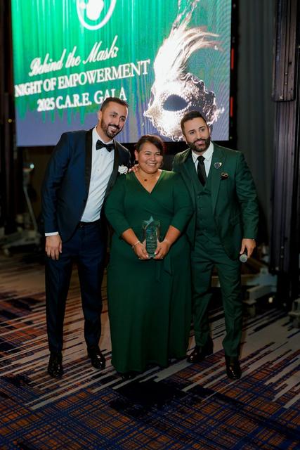 Three guests in formal wear, one holding an award, in front of a screen that reads Behind the Mask, 2025 C.A.R.E. Gala